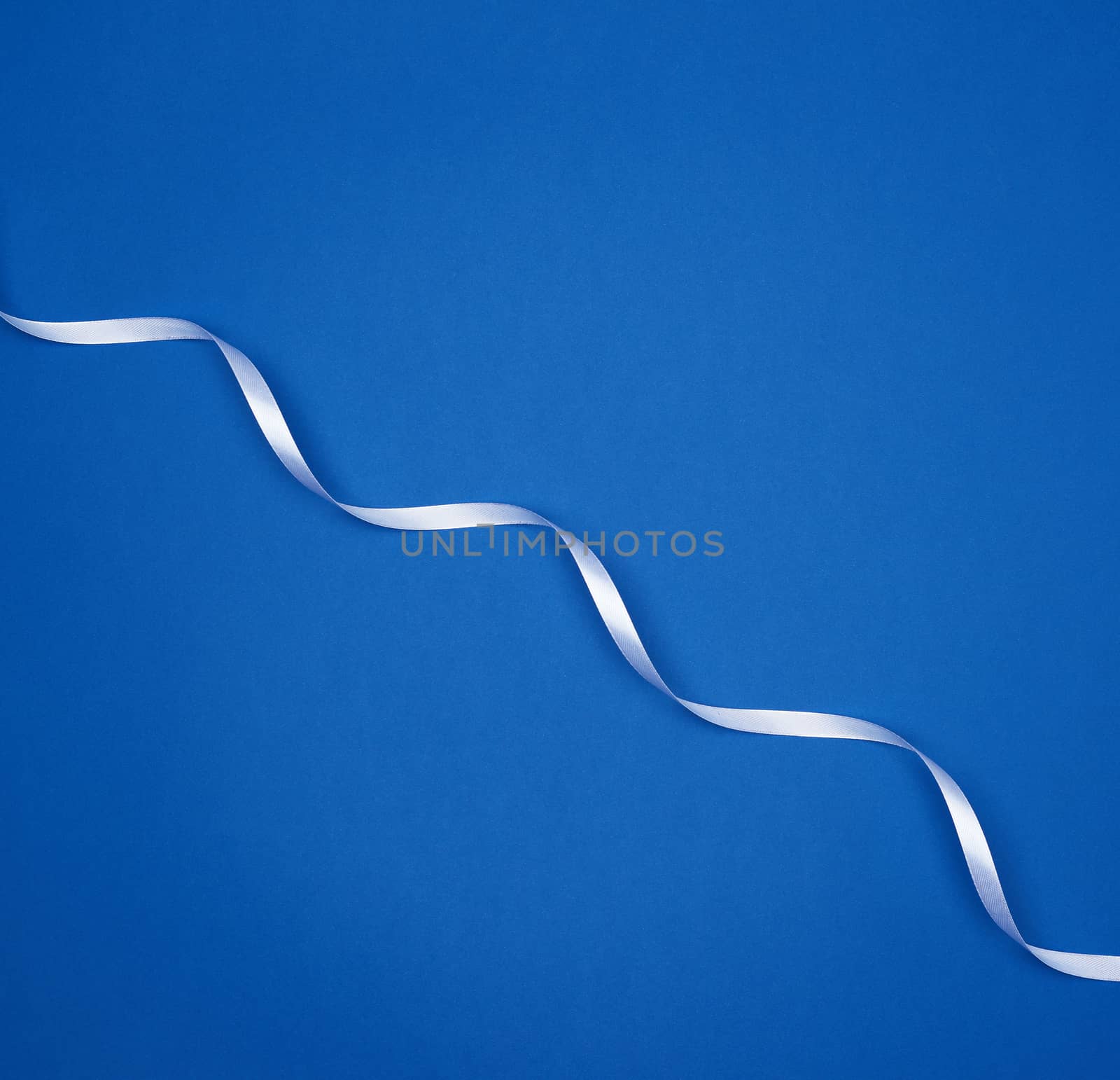 white silk thin ribbon twisted on a blue background, trendy classic color, top view