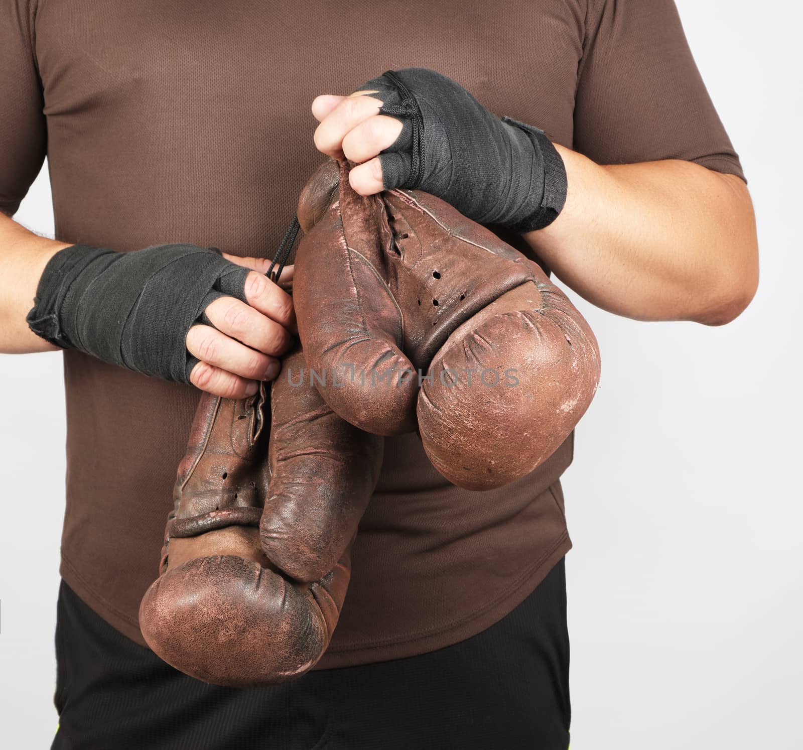 adult man in brown sport uniform holds a pair of brown vintage casual boxing gloves, white background, close up