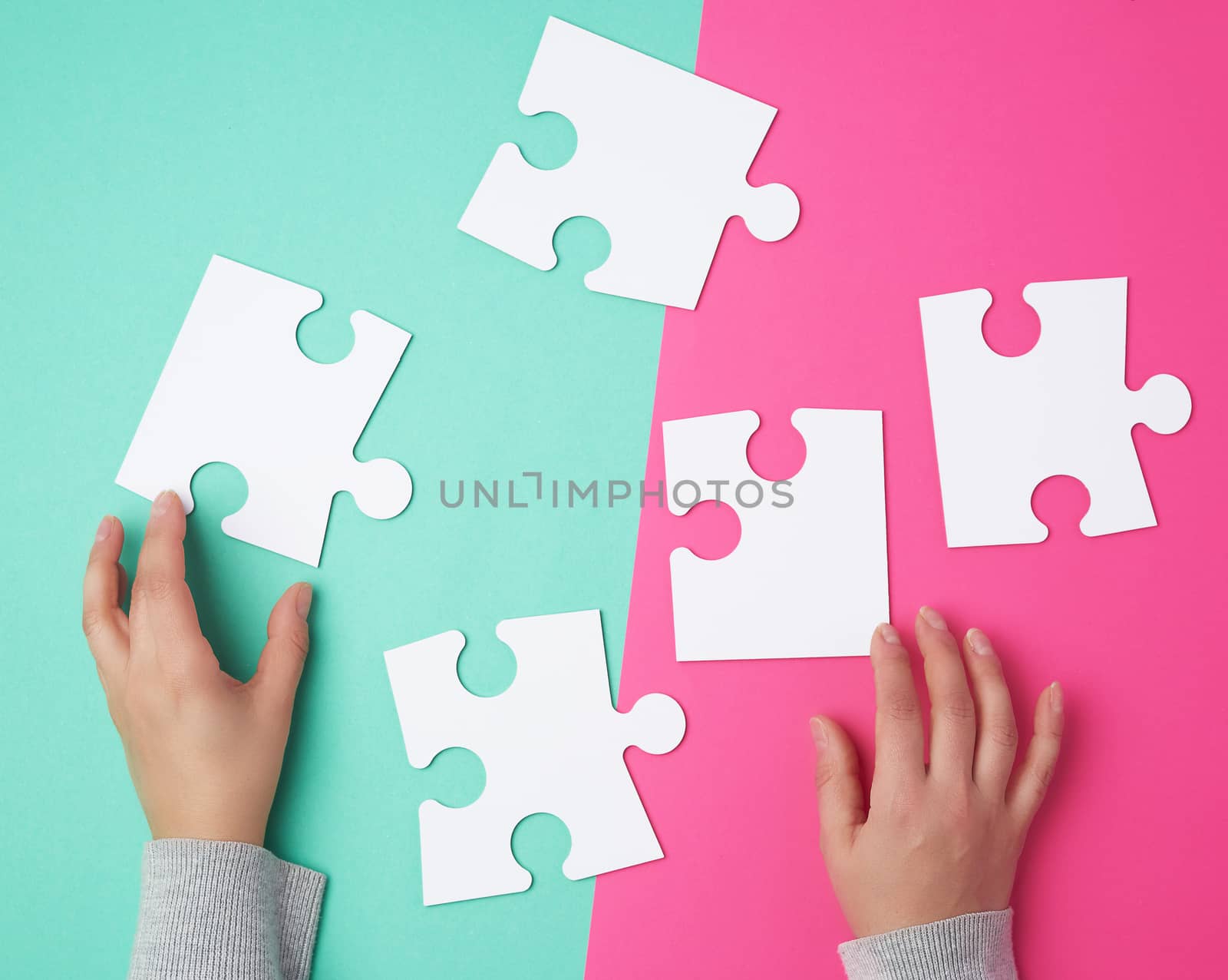 empty paper white pieces of puzzles in female hands, puzzle connected, colorful background, top view