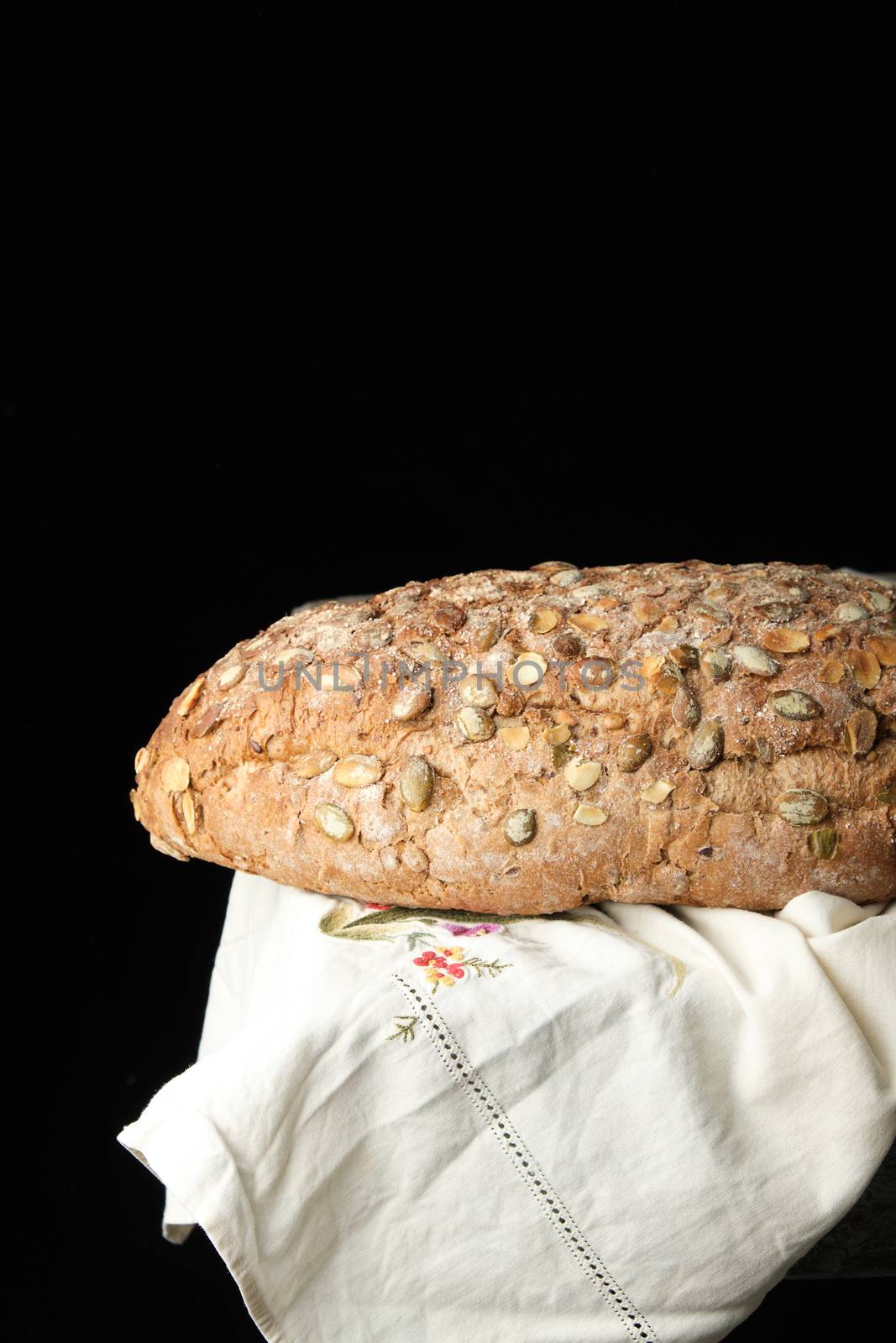 baked oval bread made from rye flour with pumpkin seeds on a white linen napkin, black  background 