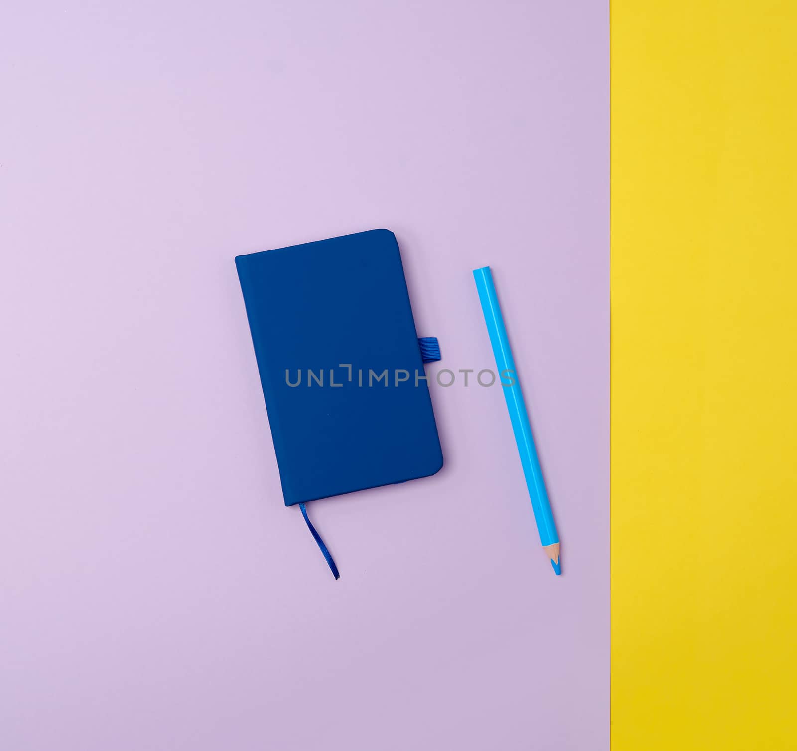 closed notebook and wooden blue pencil on a colored background, top view, flat lay