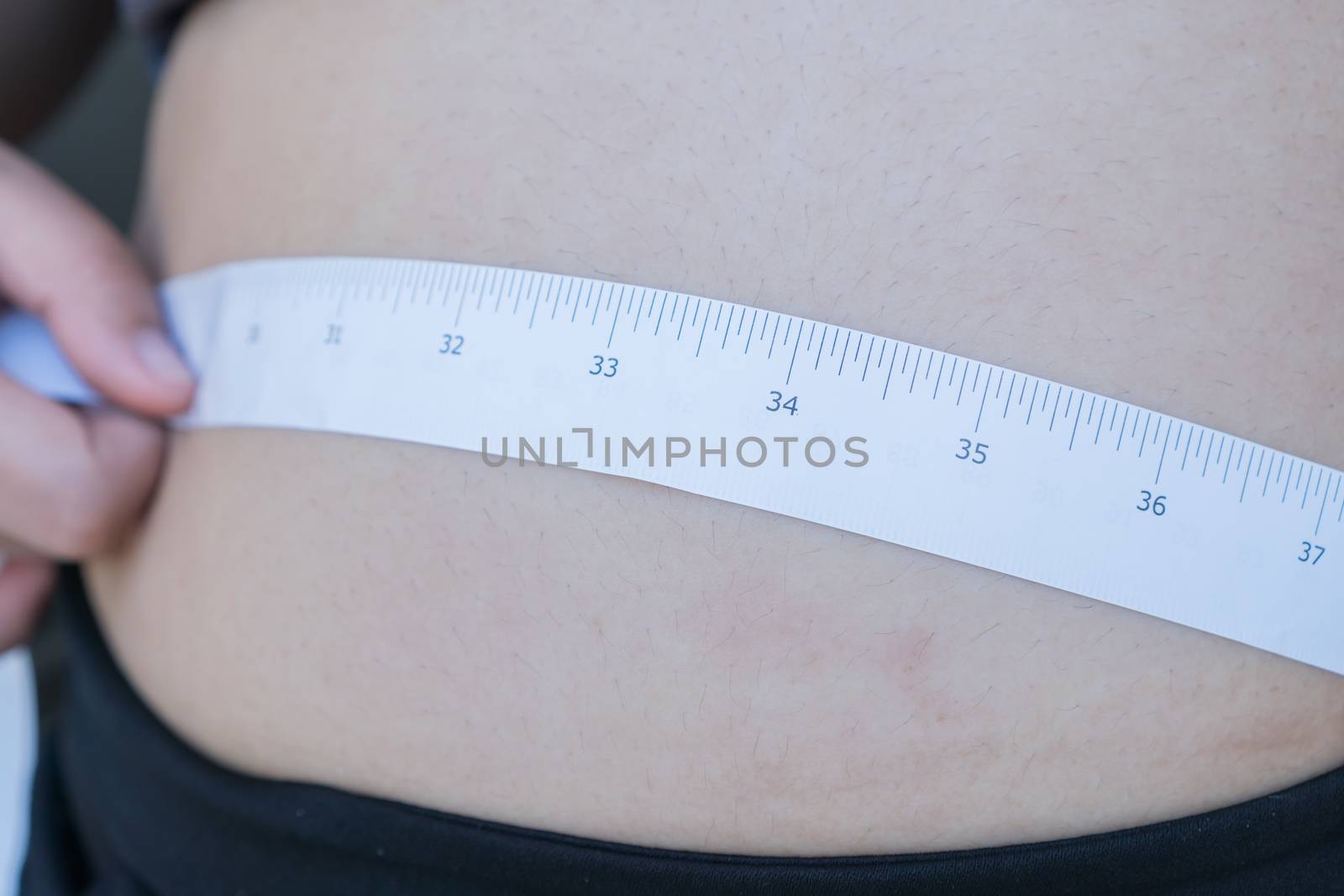 Overweight Fat Asian young woman with tape measuring her belly pinching big in sportswear, overeating problem, obesity. Weight people having more body fat than is optimally, body mass index (BMI)