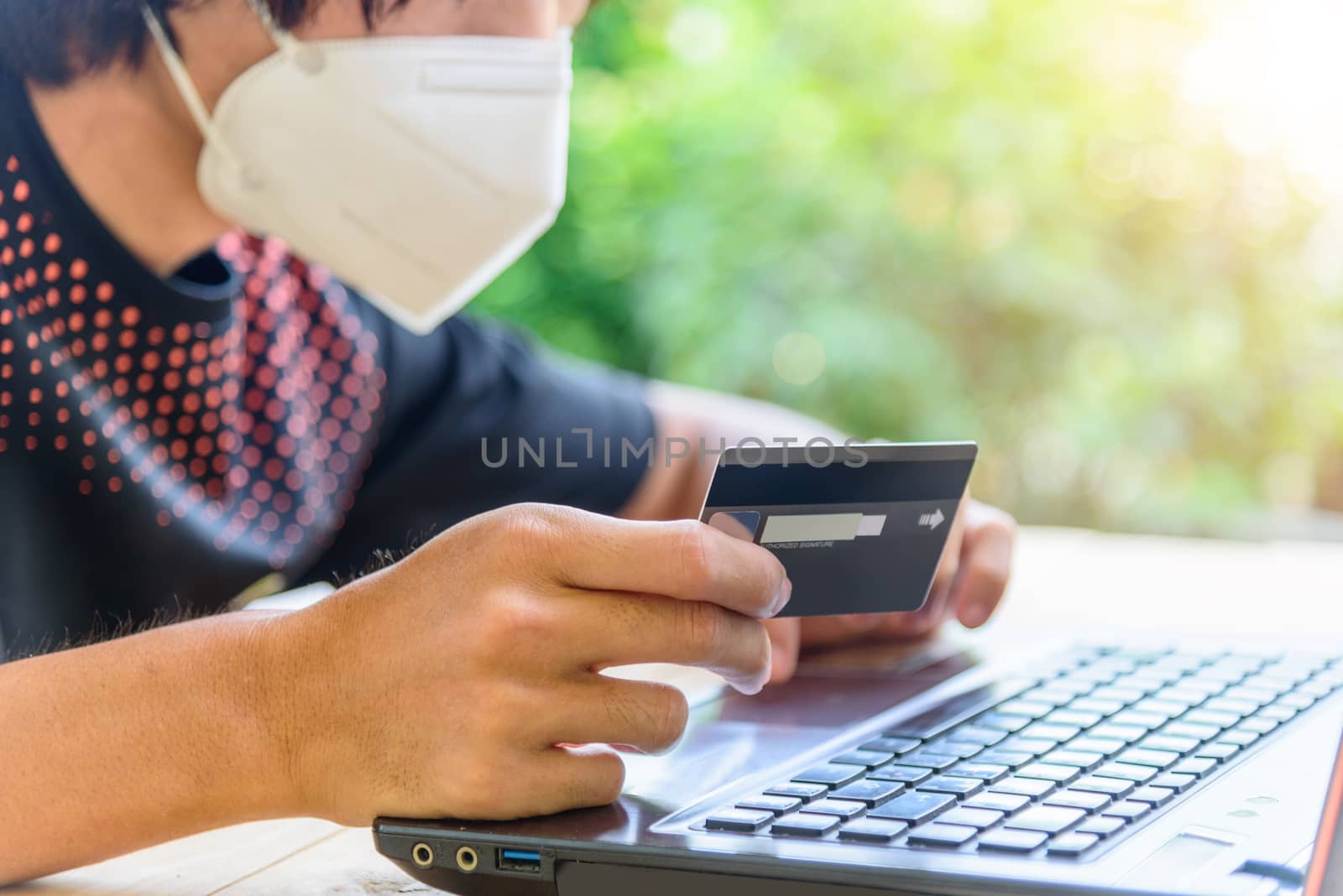 shoping from home in quarantine time/ the man wear mask and holding the credit card for shopping online in website
