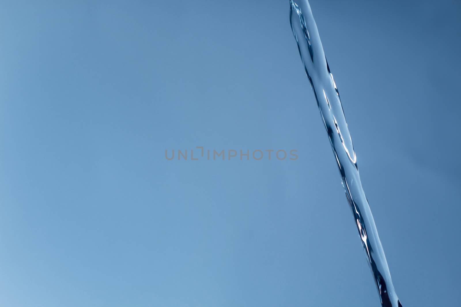 The icy stream of water against a blue background. Cold water, ice water. The glare of light is reflected in the flow of water.