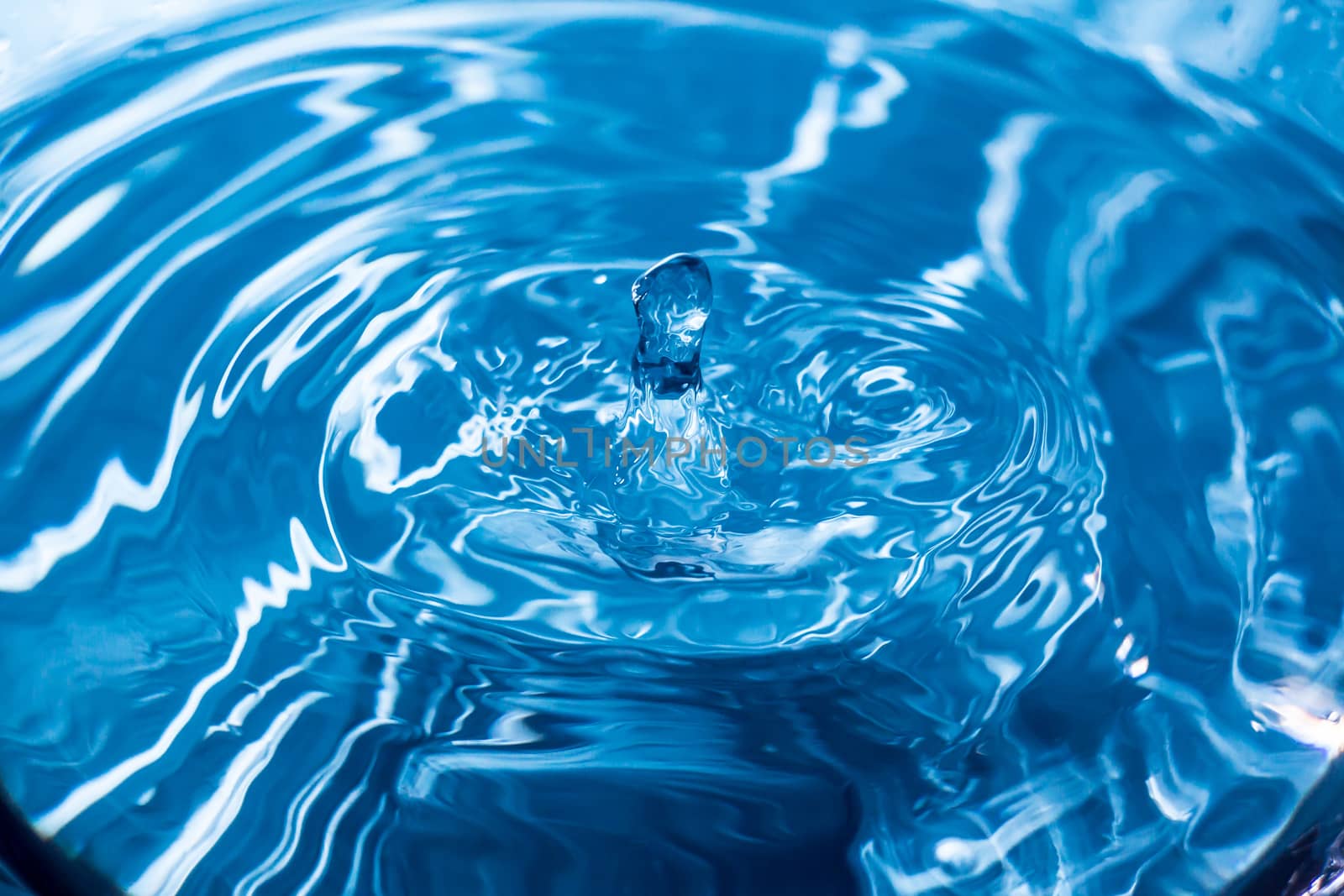 Water drops on blue surface. Water ripple background. Splashes from a drop of water. Raindrops on a blue background. The texture of the water. Aqua, turquoise, macro