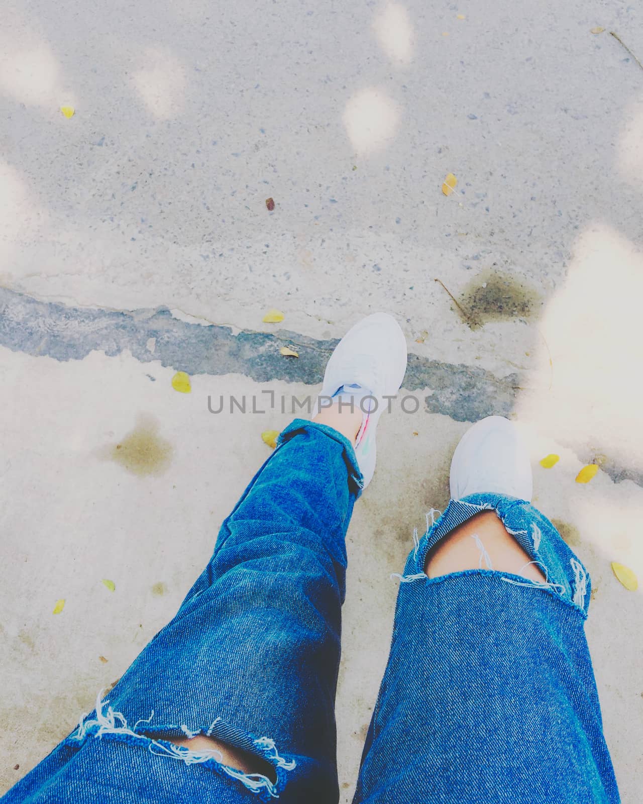 Woman's legs with blue fashion jeans and white sneakers on street by iamnoonmai