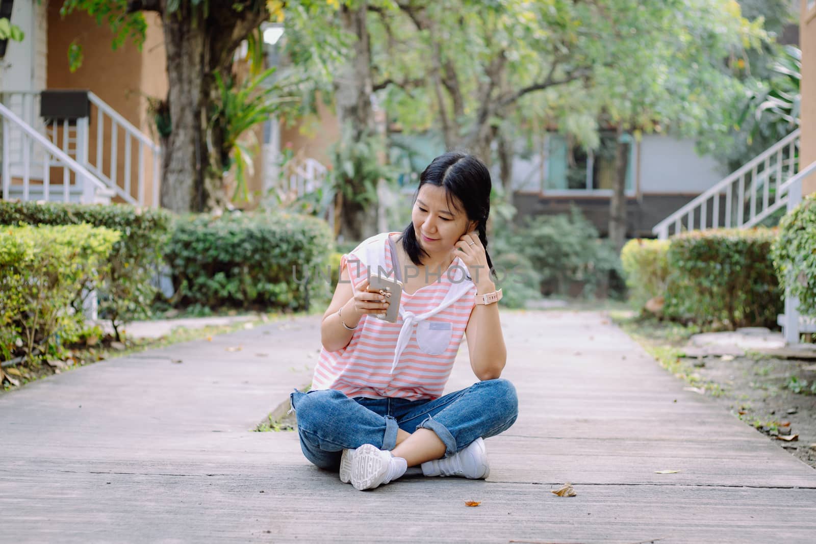 Young asian woman in casual clothes using smartphone and sitting on the road for communication and technology concept