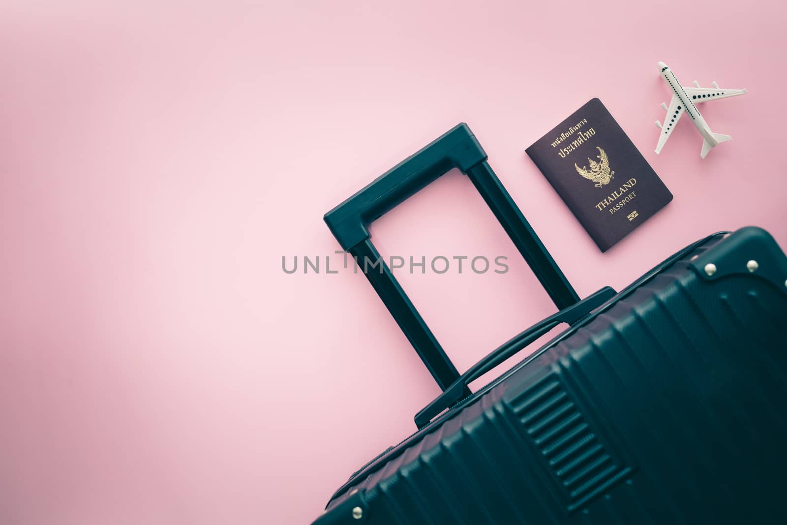 Black luggage, Thai passport and white airplane model on pink background for travel and journey concept