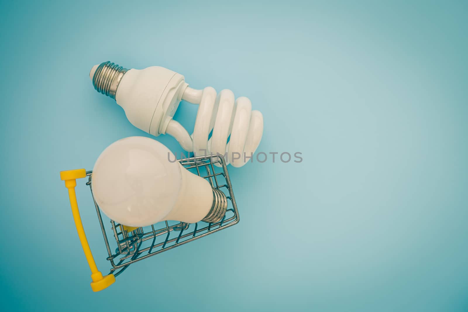 Fluorescent and LED light bulb with mini shopping cart or trolley on blue background for energy savings concept