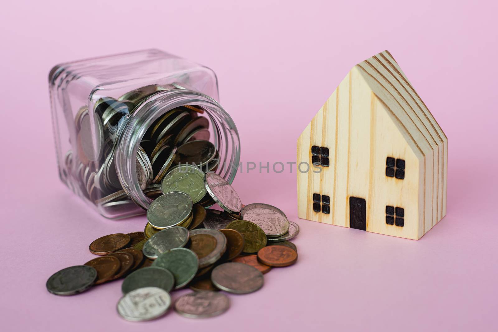 Wooden house model with money coins in the glass jar on pink background with copy space for business and finance for property concept
