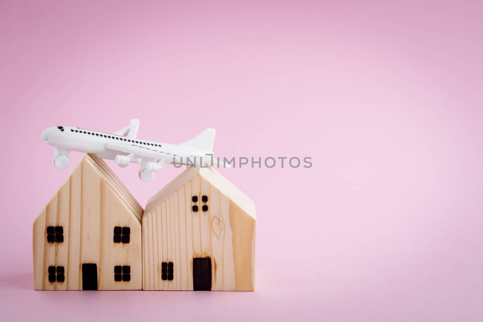 White airplane and wooden house model on pink background for travel concept