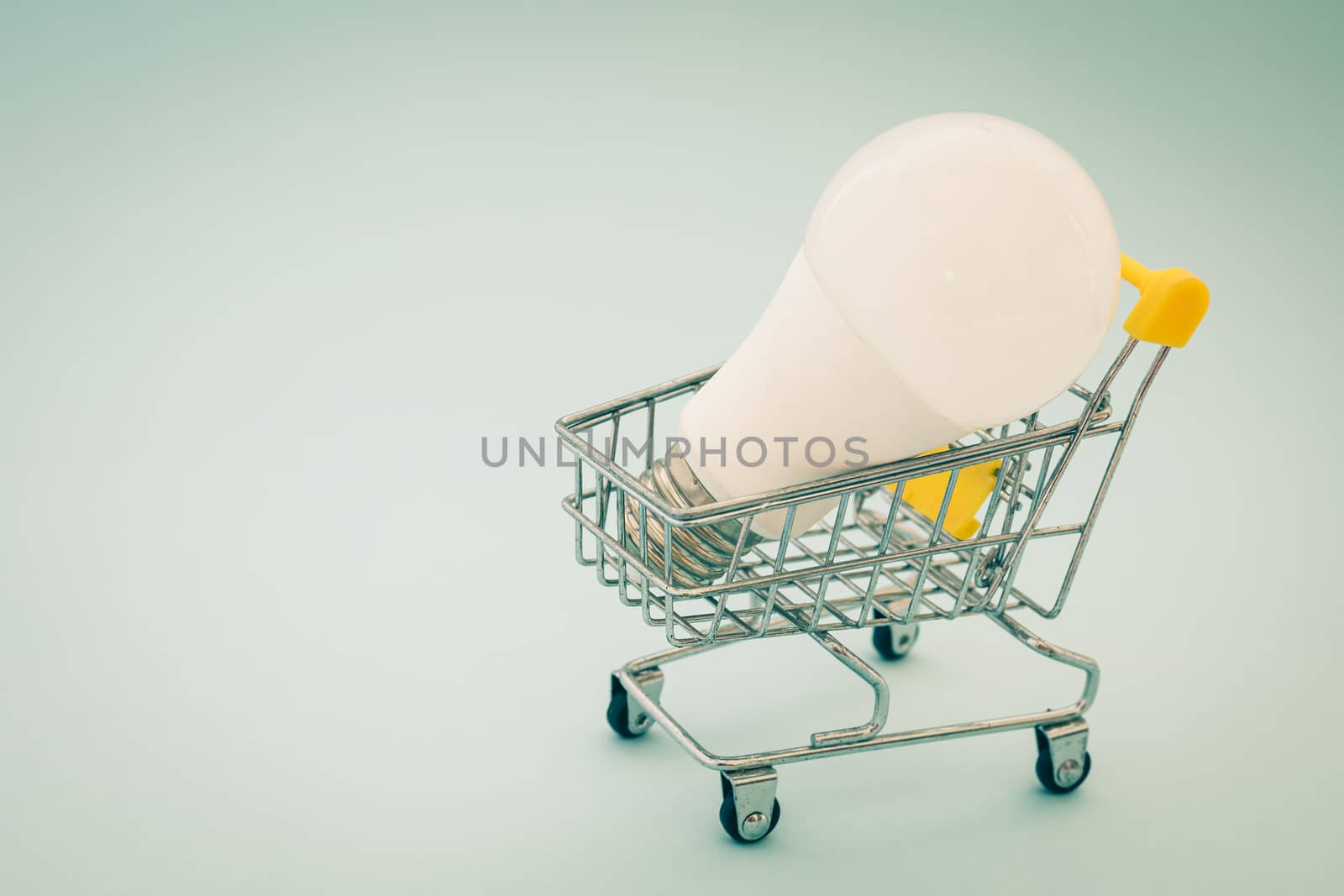 Glowing LED light bulb with mini shopping cart or trolley on blue background for energy savings concept