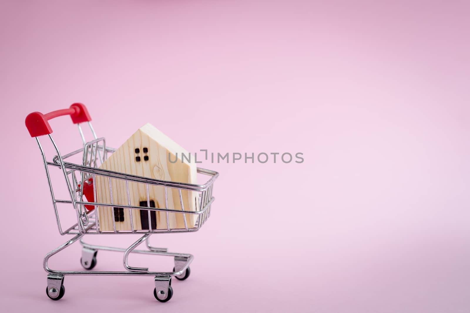 Wooden house model in the shopping cart on pink background for housing and property concept