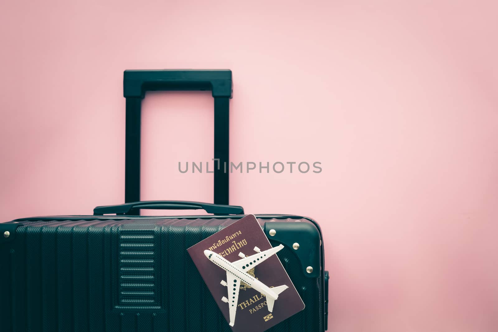White airplane model, Thai passport and black luggage on pink background for travel and journey concept