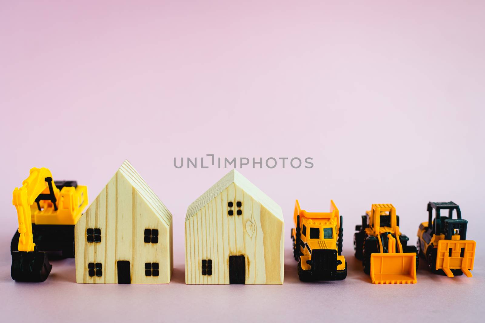 A yellow toy heavy machinery with wooden house model on pink background for housing and construction concept