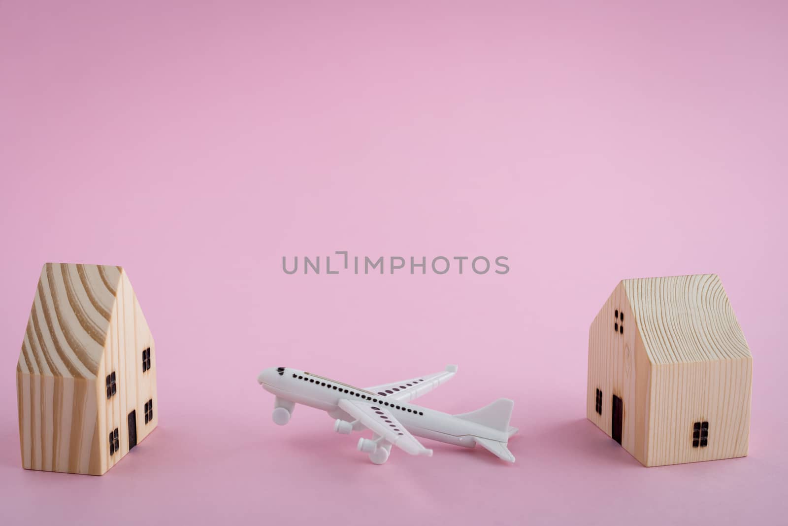 White airplane and wooden house model on pink background for travel concept