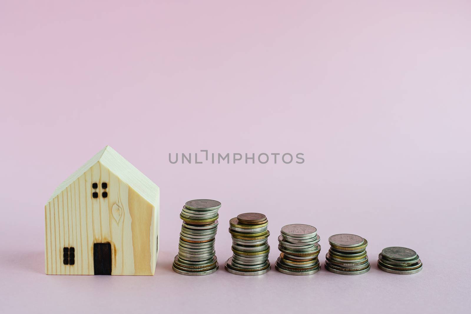 Wooden house model with step of money coins on pink background with copy space for business and finance for property concept