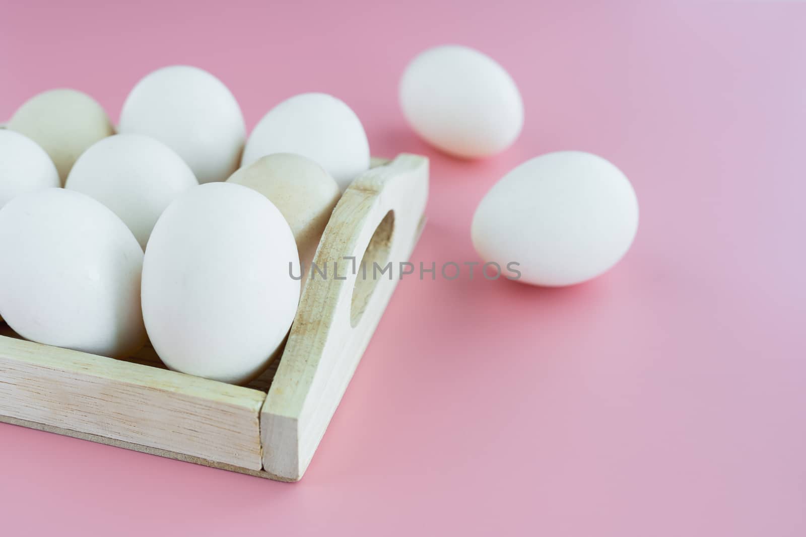 White eggs in the wooden tray on pink background for healthy food concept