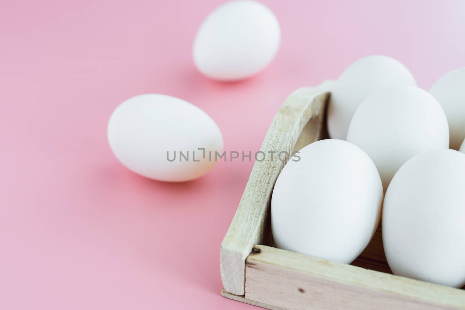 White eggs in the wooden tray on pink background for healthy food concept