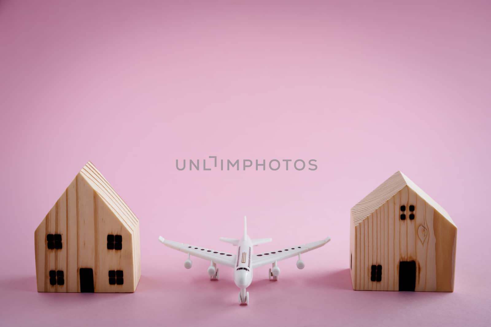 White airplane and wooden house model on pink background for travel concept