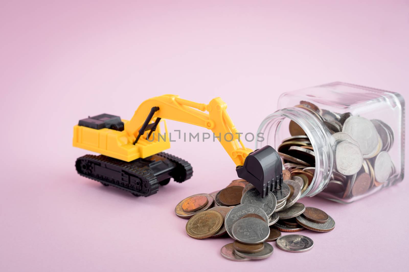 The excavator loader model with pile of coins in the glass jar on pink background for saving money, investment, business and finance concept