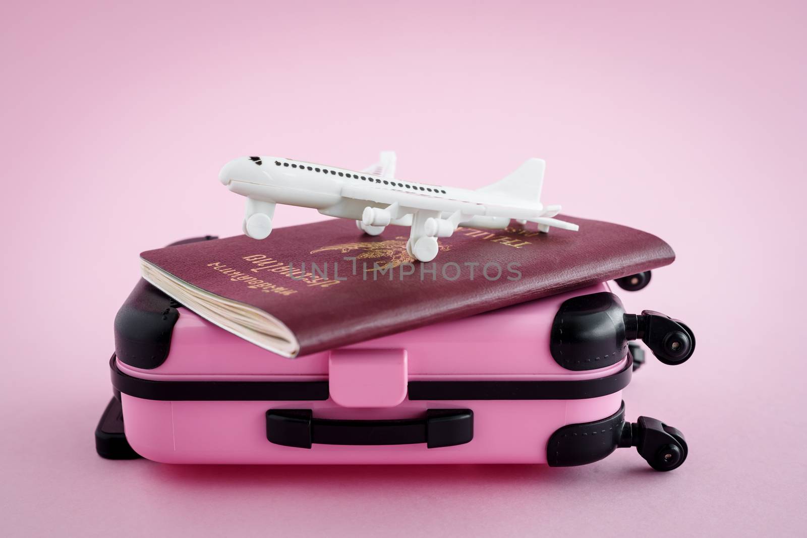 Pinky luggage with Thai passport and white airplane model on pink background for travel and journey concept