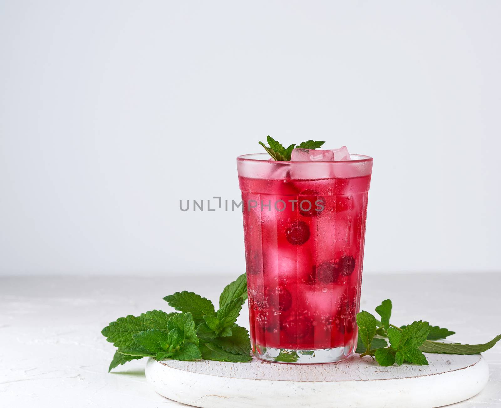 summer refreshing drink with red berries of cranberries and pieces of ice in a glass on a wooden board, white background