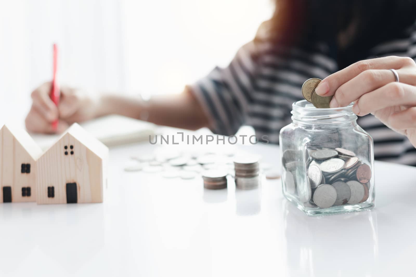 Woman's hand saving a coin into the glass jar for planning, housing and property financial concept