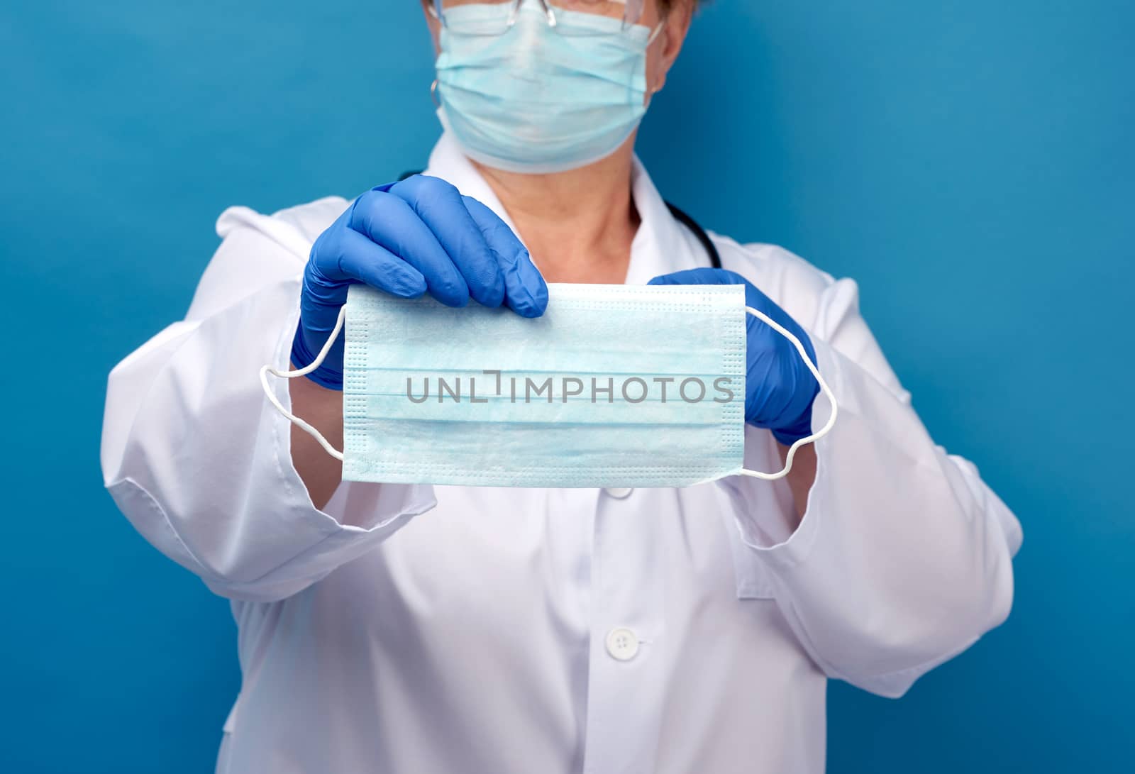 doctor in a white coat and mask holds a stack of protective disposable face masks, physician stands on a blue background