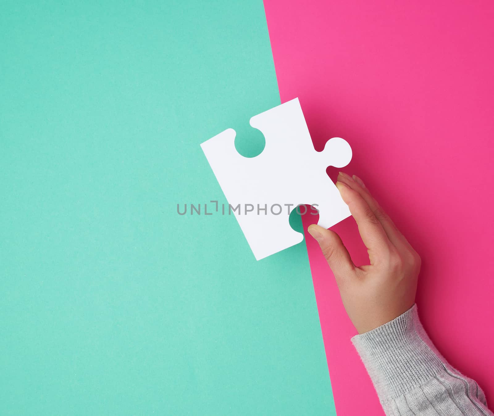 female hand holds a big empty white puzzle over a colorful background, place for text