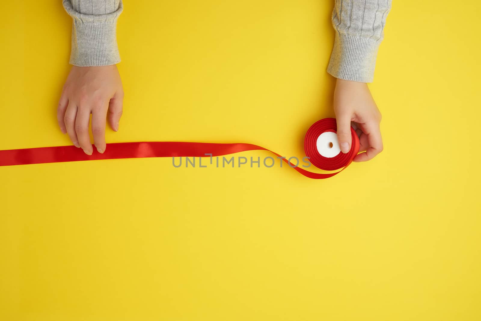 two female hands and red ribbon on a yellow background, top view