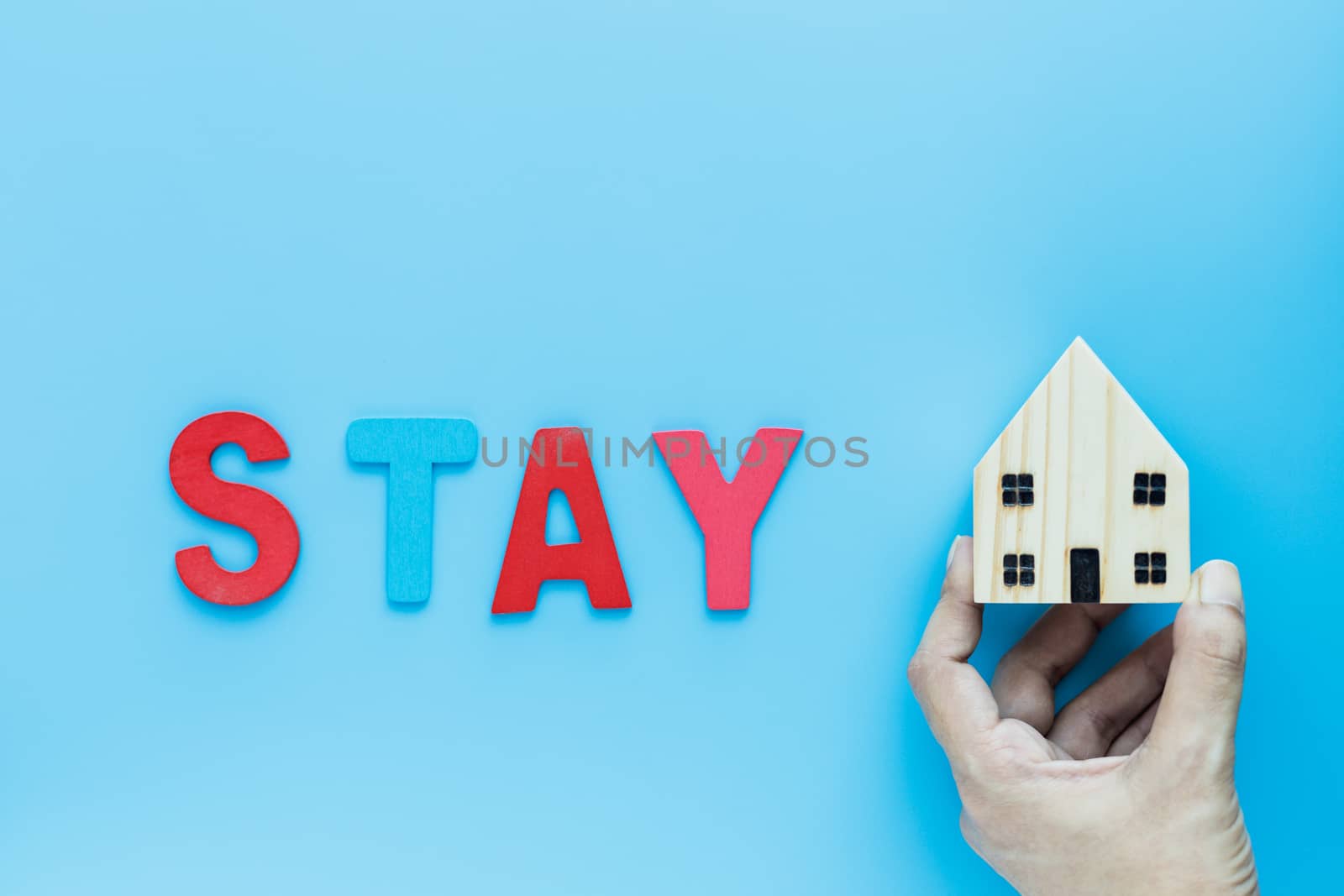 Hand holding wooden house model with STAY text on blue background for self-quarantine, staying home and social distancing in coronavirus or Covid-2019 situation concept