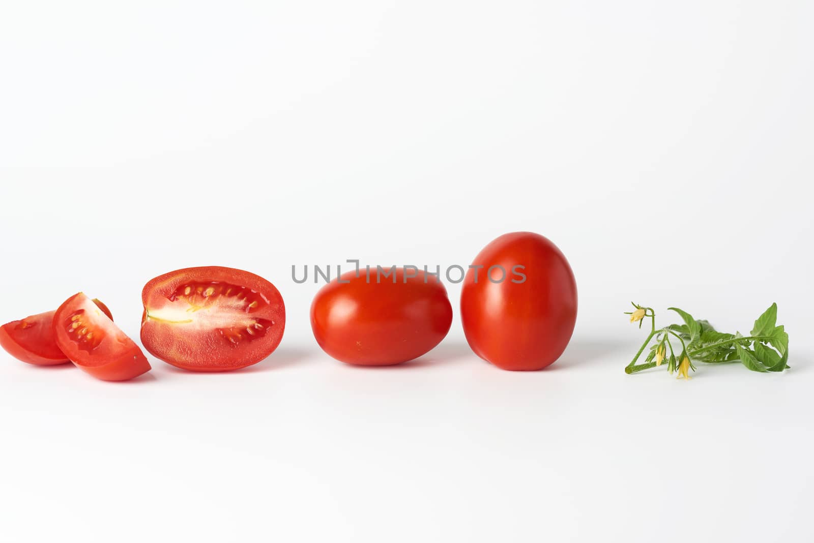 ripe red whole tomatoes and slices, green leaf on a white background, autumn harvest for salad and cooking