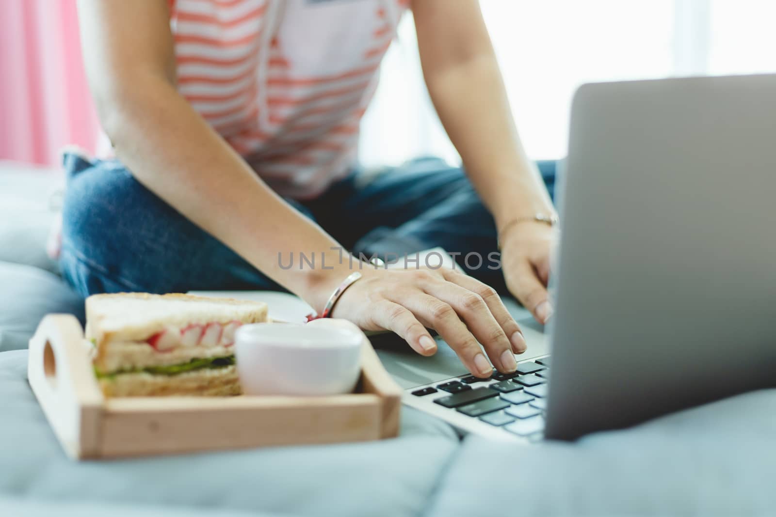 Woman using computer and having breakfast in bed for self-quarantine, social distancing, staying and working at home in coronavirus or Covid-2019 outbreak situation concept