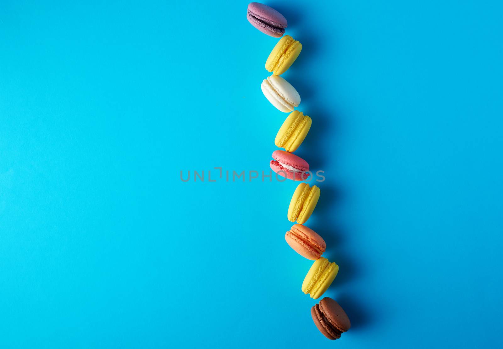 round multi-colored baked macarons with cream lie in a line on a blue background, flat lay, copy space
