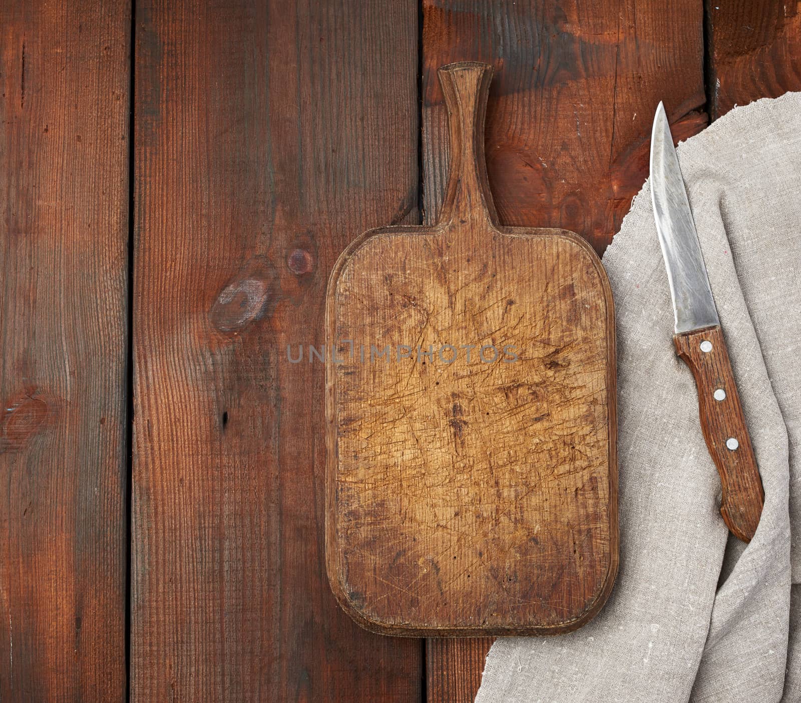 very old empty wooden rectangular cutting board and knife, top view, brown wooden background 