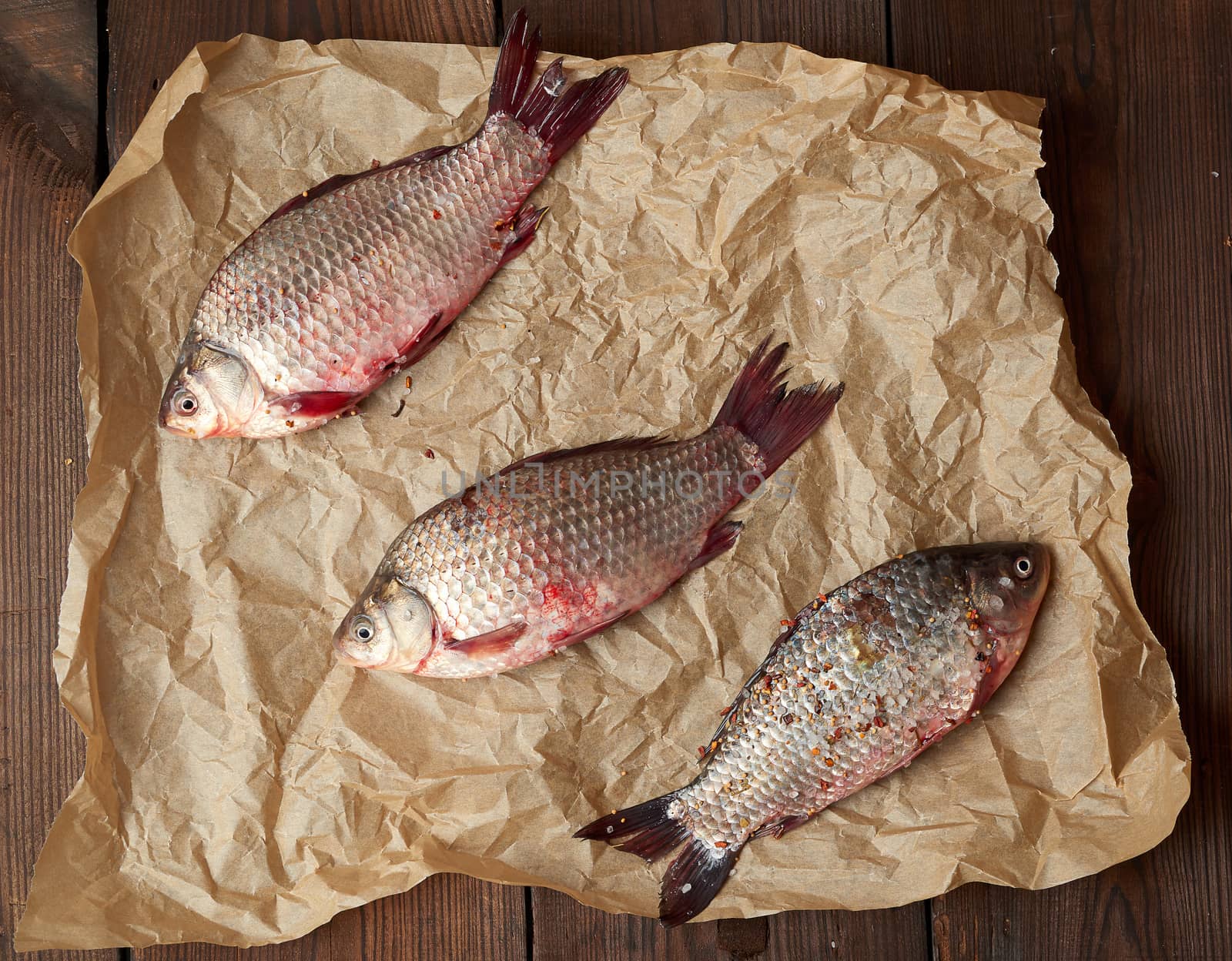 whole fresh crucian fish with scales on a crumpled brown piece of paper, top view