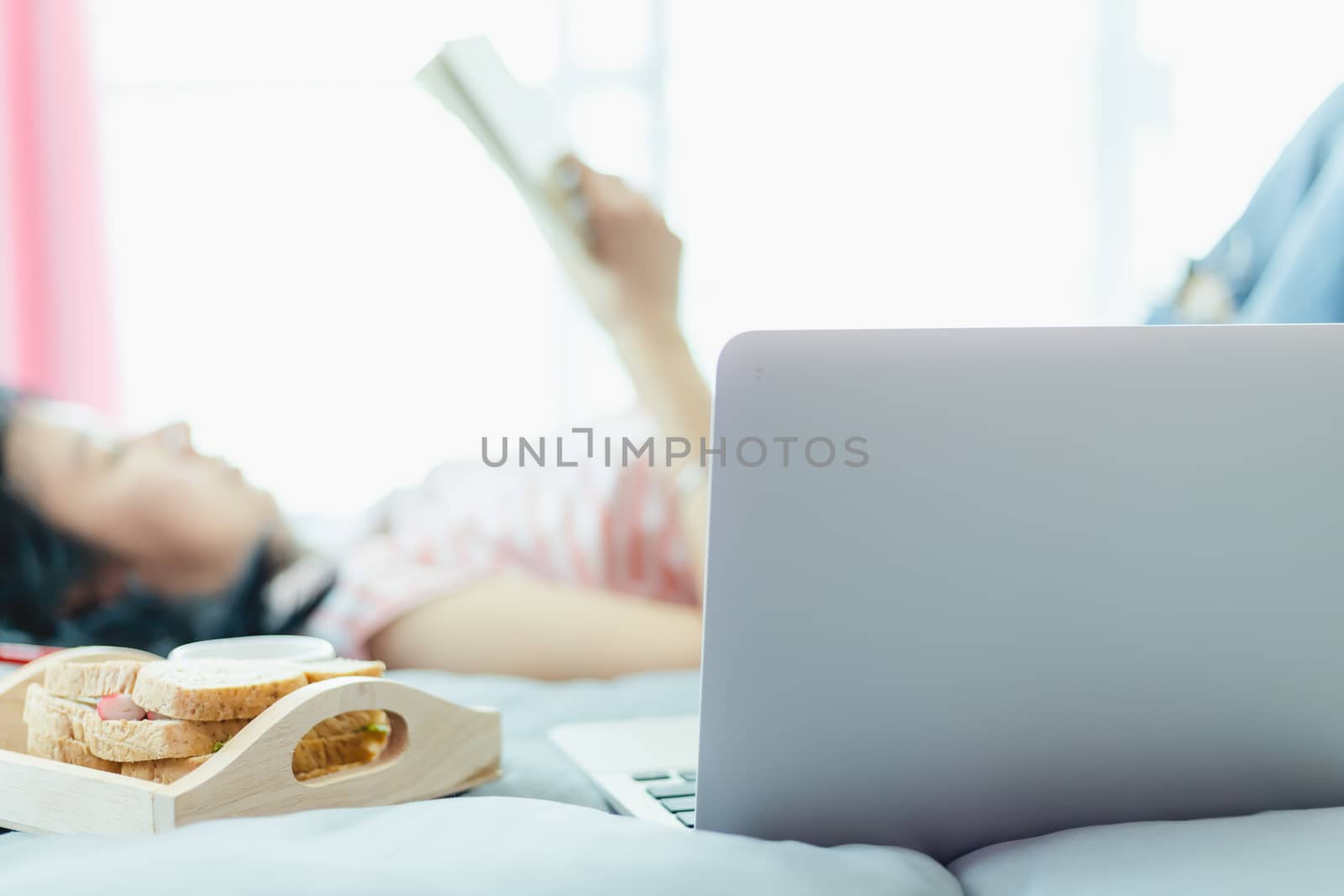 Blurred woman reading a book with computer and breakfast in bed for self-quarantine, social distancing, staying and working at home in coronavirus or Covid-2019 outbreak situation concept