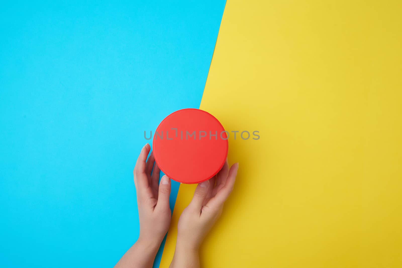 two female hands hold a closed paper cardboard box on a yellow-blue background, concept of surprise
