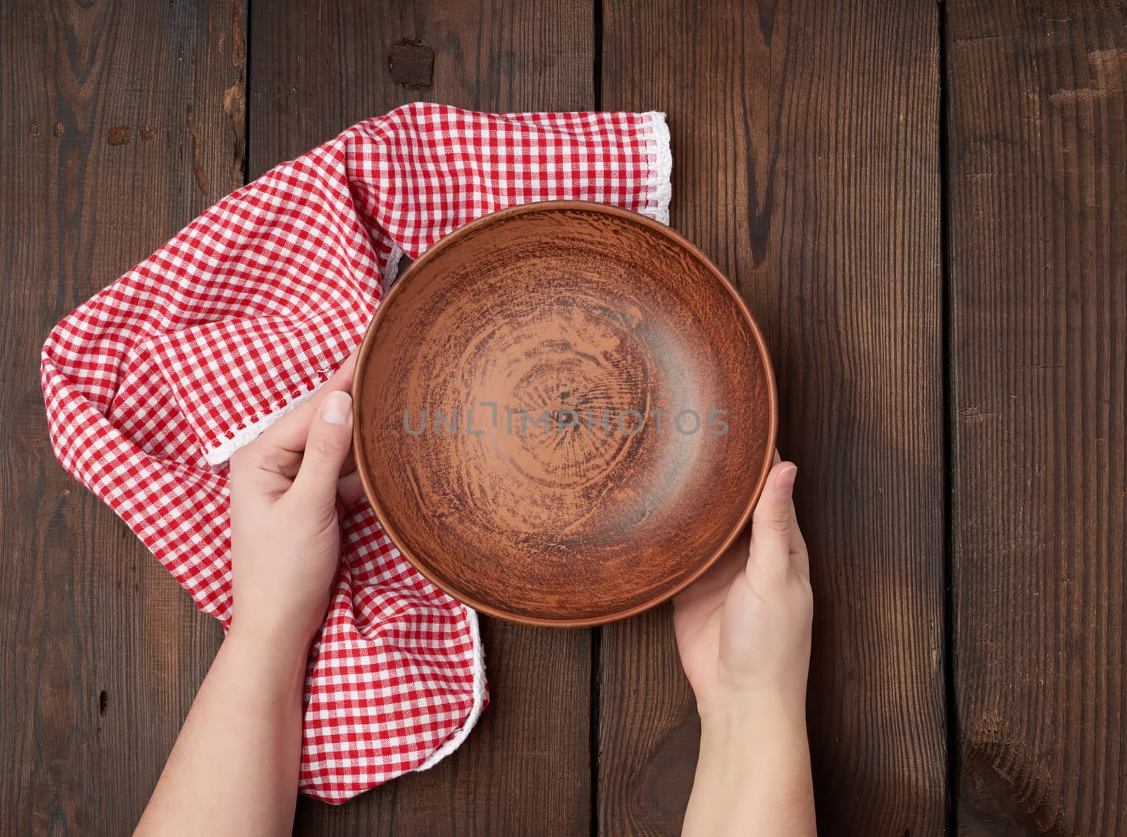 two female hands holding an empty round clay plate, top view