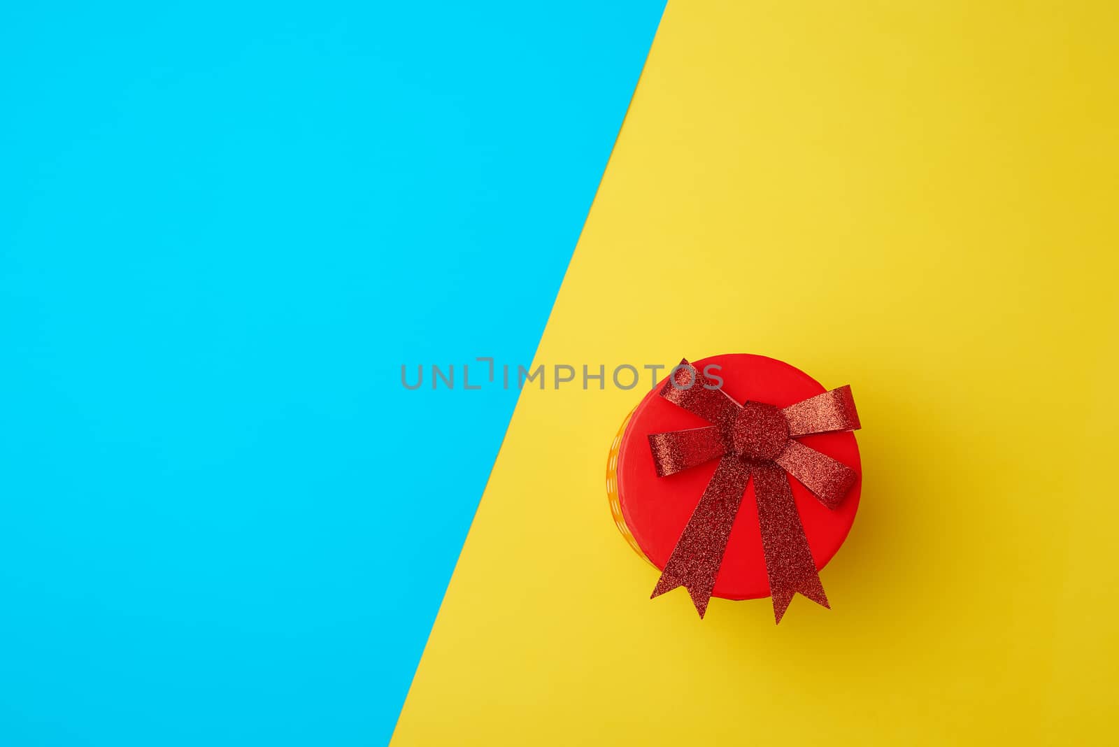 round cardboard red box with a bow on a blue-yellow background, top view, place for text