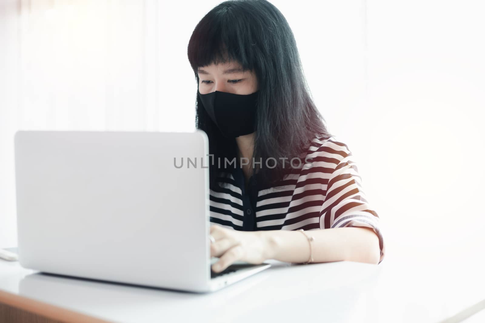 Woman wearing a black face mask, using laptop and working at home for business, self-quarantine, staying home and social distancing in coronavirus or Covid-2019 outbreak situation concept