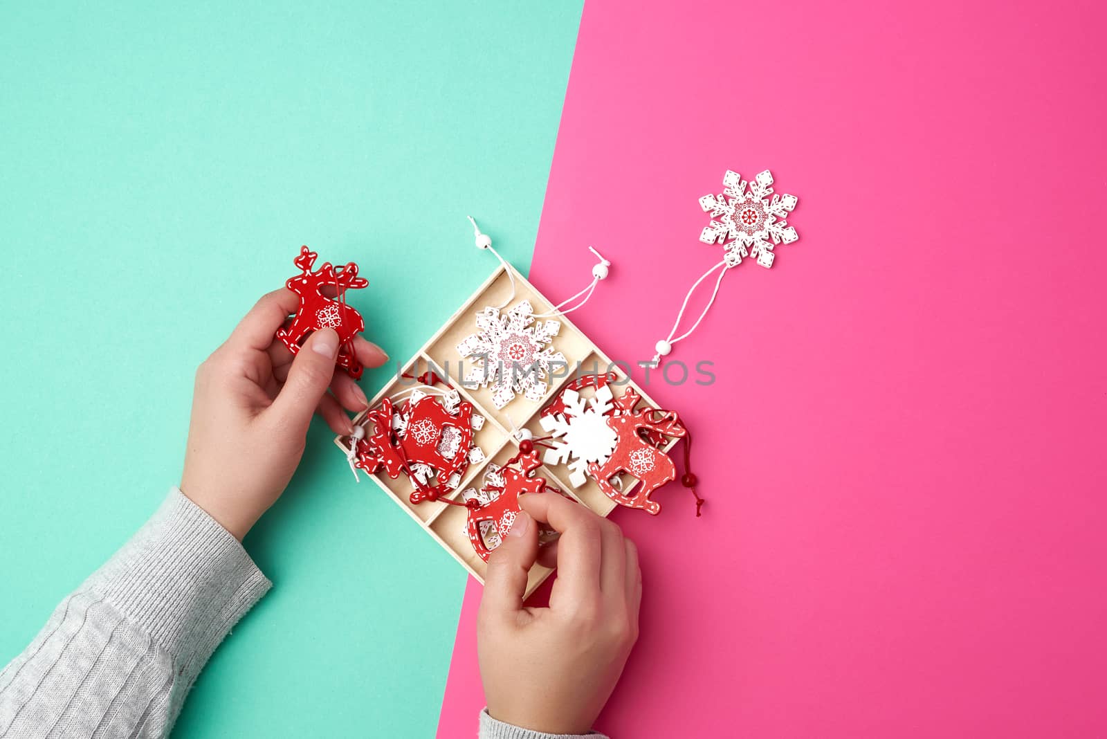 two female hands and wooden carved Christmas decorations for the holiday tree, pink green background 