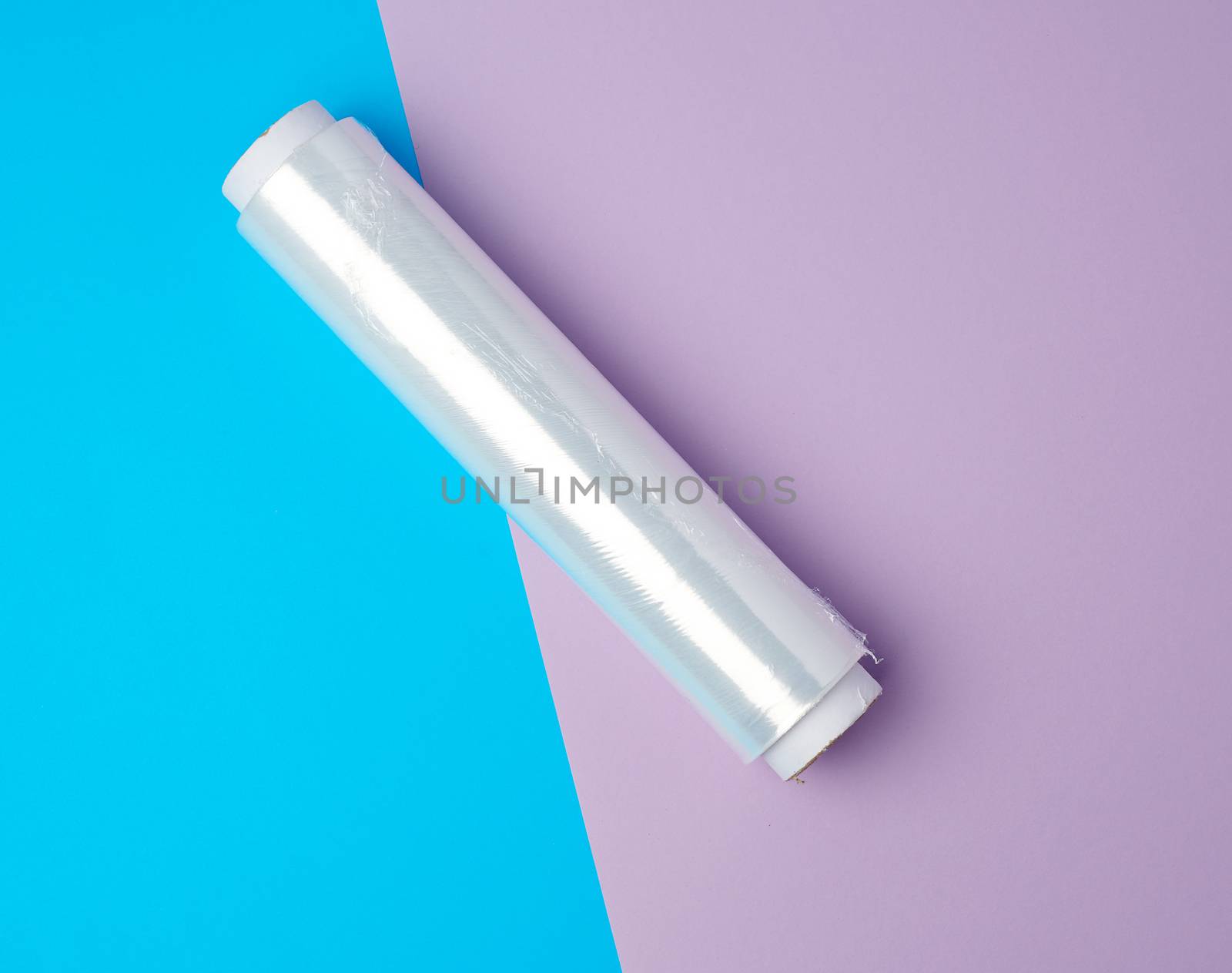 roll with transparent white polyethylene for wrapping products and packaging goods on a colored background, top view