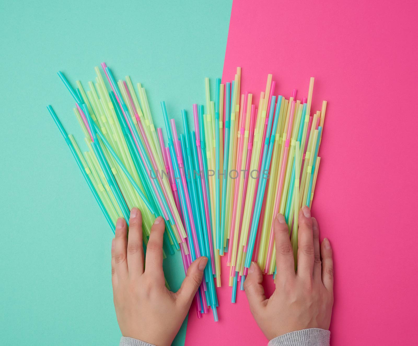 female hand holding multicolored plastic cocktail tubes, green pink background