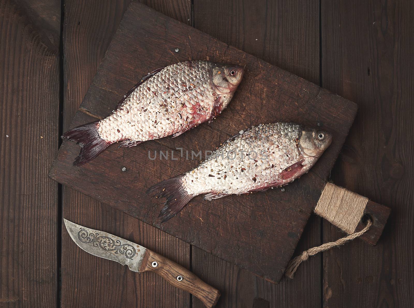 fresh crucian fish lies on a brown wooden cutting board, wooden table from boards, top view