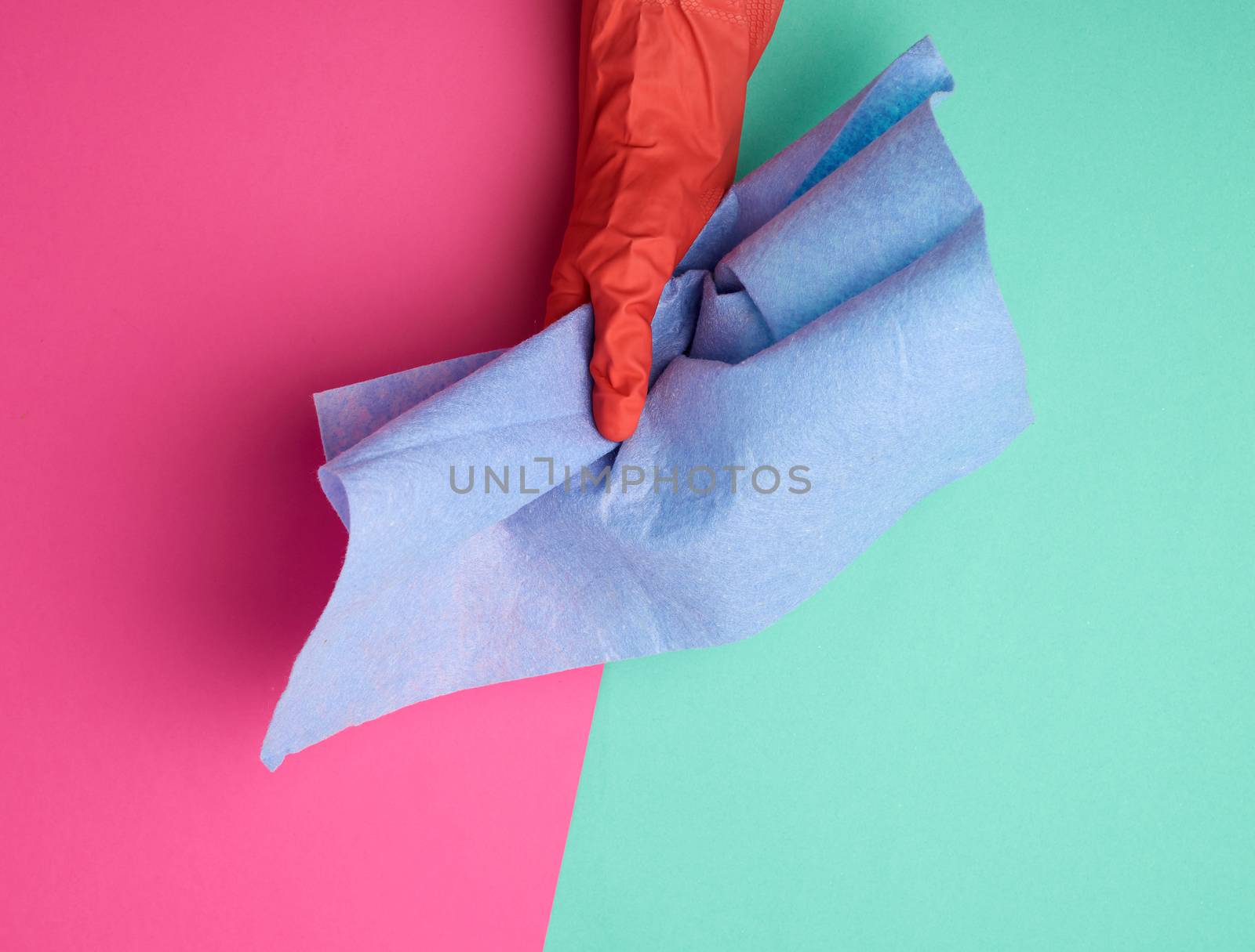 blue viscose rag for cleaning dust in the house in hands with an orange glove on, colored background