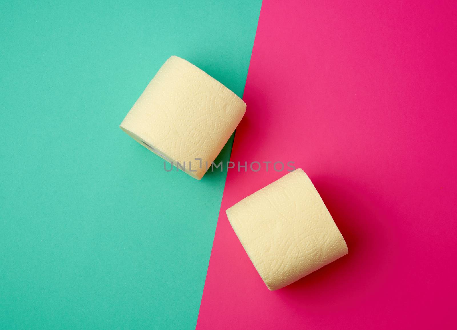soft yellow toilet paper in a roll on a green-pink background, top view
