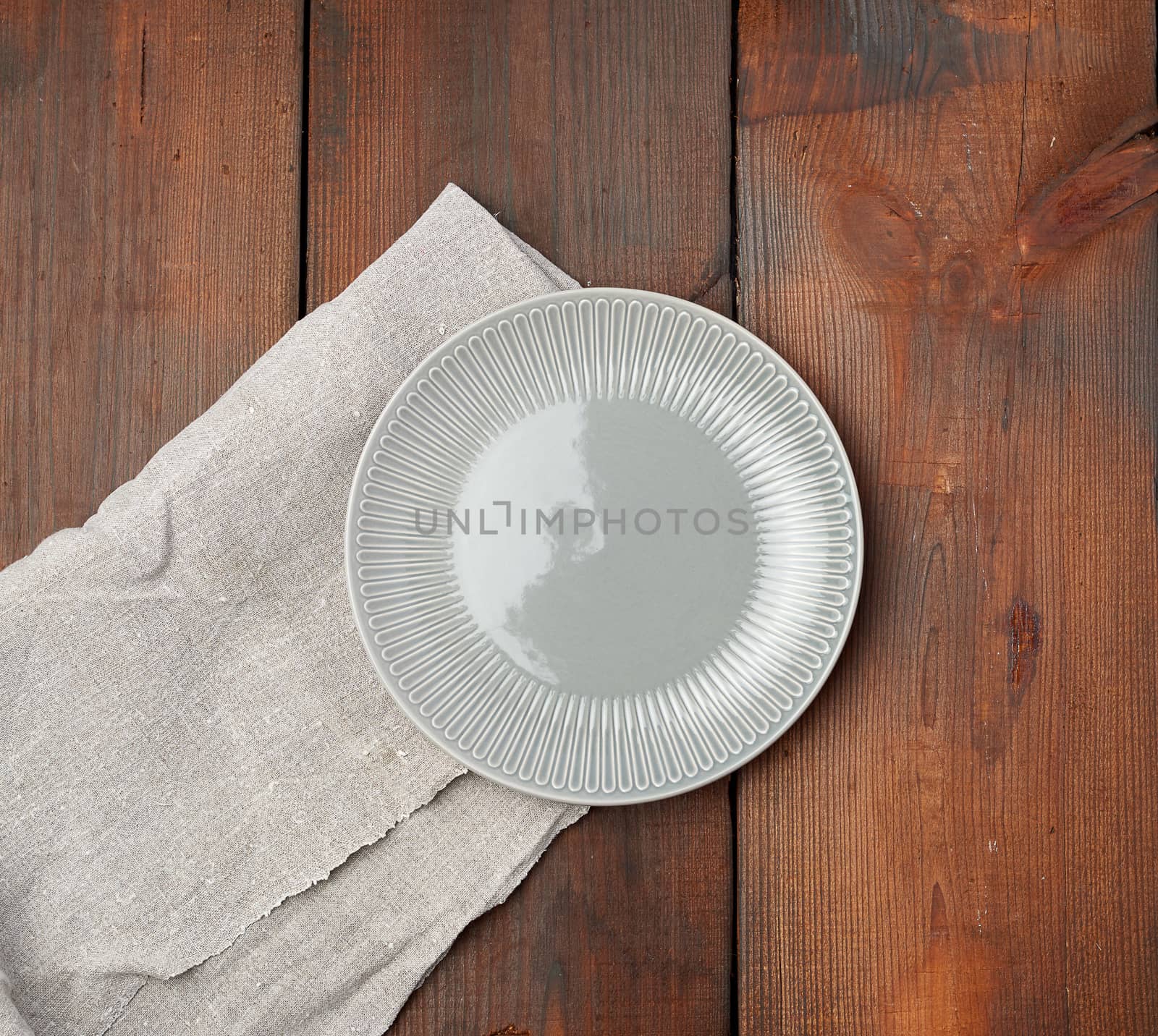 empty gray round ceramic plate stands on a linen napkin, wooden background, top view