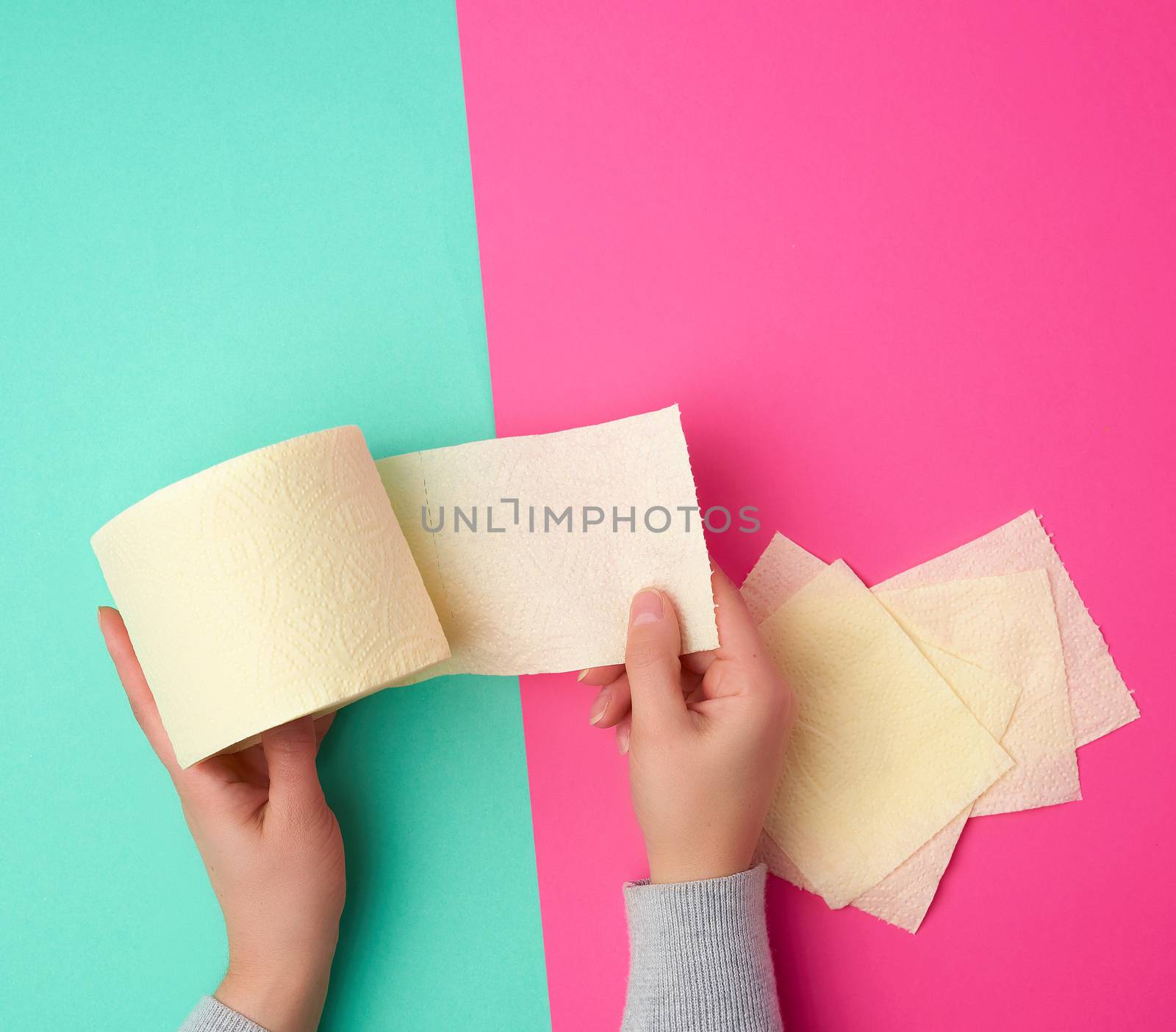 roll of yellow toilet paper in female hands, torn pieces on a colored background, top view
